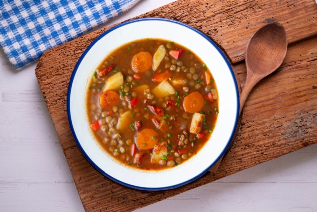 7 sopas ricas em proteínas para começar a semana 6 Sopa de lentilhas picantes com legumes e batatas em prato branco com borda azul