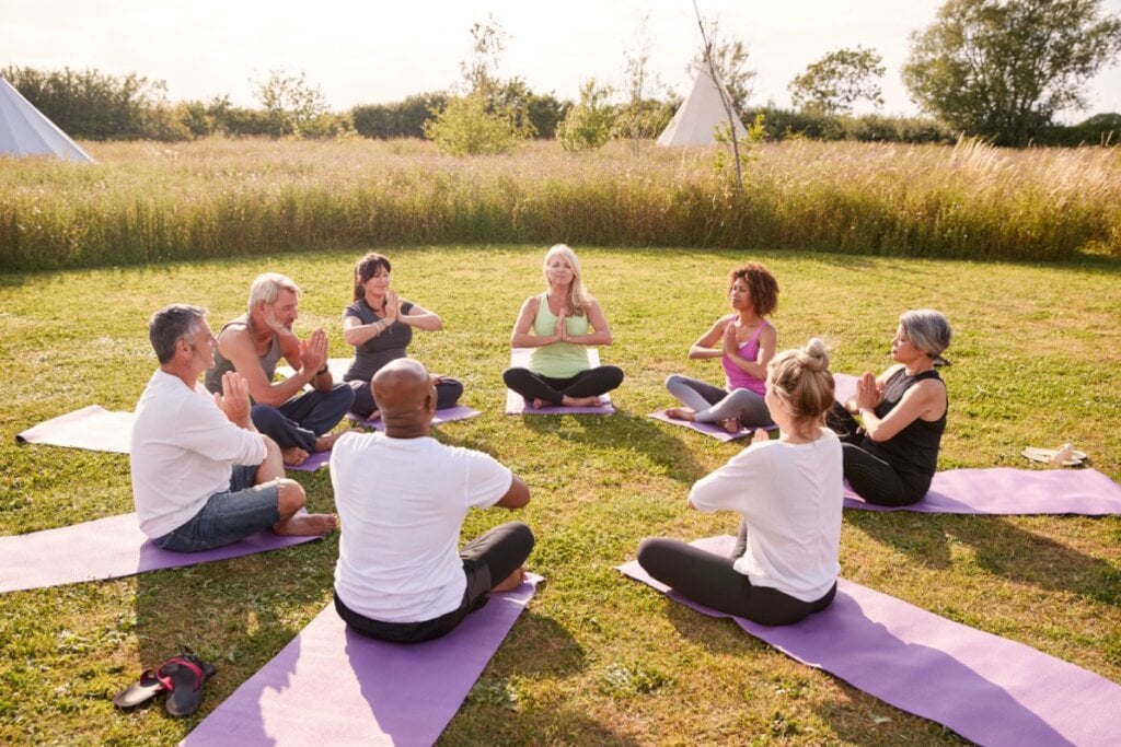 11 benefícios da meditação para a saúde 6 Pessoas reunidas em uma roda, ao ar-livre, fazendo meditação