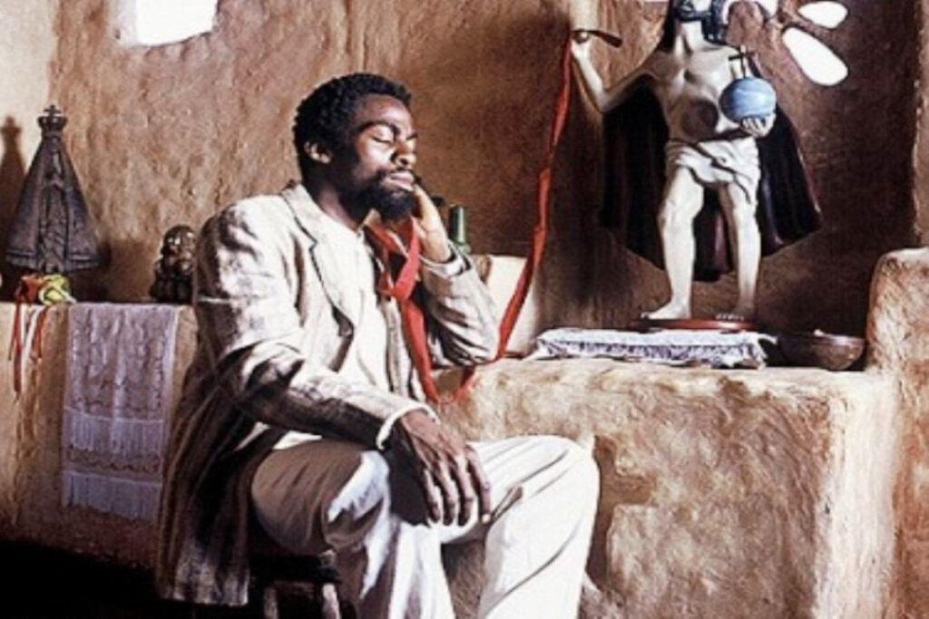 7 filmes essenciais sobre escravidão no Brasil e no mundo 31 Cena do filme "Cafundó" com homem negro sentado, com os olhos fechados e cotovelo em mesa de pedra