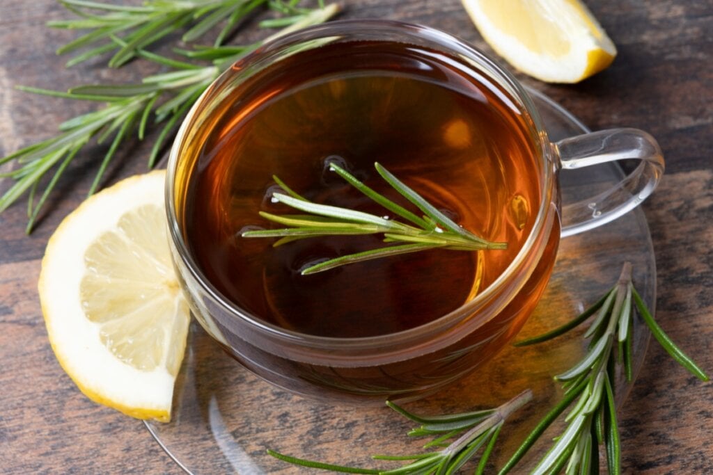 8 receitas de chás funcionais para o inverno 6 xícara de vidro com chá marrom com alecrim. ramos de alecrim e fatias de limão em volta