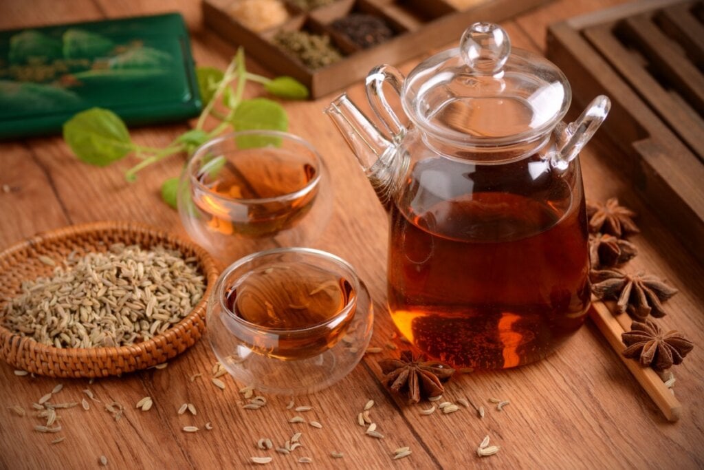 7 chás deliciosos e práticos para os dias frios 6 Chá de erva-doce com anis-estrelado em bule de vidro e servido em dois copos de vidro em cima de mesa de madeira, com sementes de erva-doce e anis-estrelado espalhados na mesa