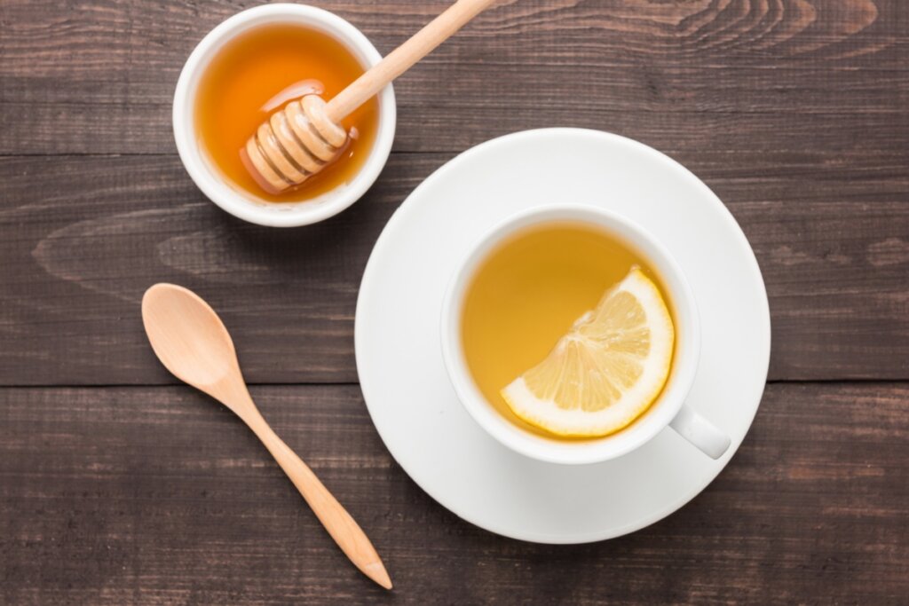 8 receitas de chás detox para os dias frios 6 Chá de limão-siciliano com mel em xícara branca em cima de pires branco ao lado de colher e recipiente com mel