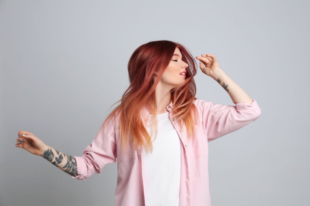 5 cores para transformar o cabelo para o inverno 23 mulher de camiseta branca e camisa rosa balançando o cabelo ruivo rosado