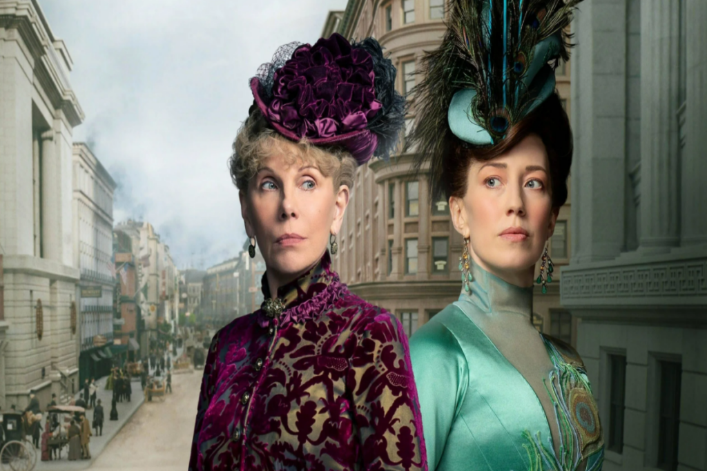 5 filmes e séries que estreiam na Max em junho de 2025 24 Duas mulheres uma ao lado da outra e atrás uma imagem da cidade de Nova York, ambas estão vestidas com roupas de época, uma em tons de roxo e outra em tons de verde