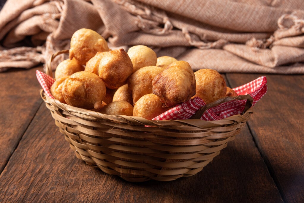 7 receitas de bolinho de chuva para as tardes frias 6 Bolinho de chuva de fubá em uma cesta de palha com pano quadriculado vermelho e branco