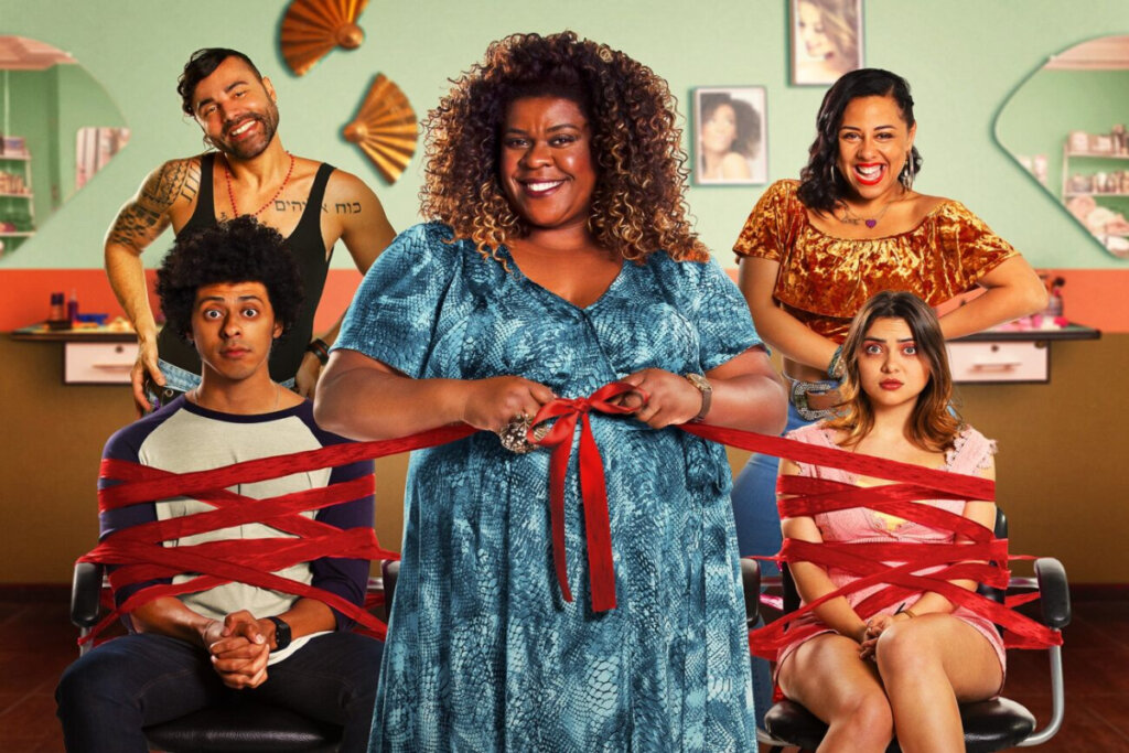 6 filmes de comédia sobre mães brasileiras 29 imagem com mulher no centro com vestido azul, duas pessoas atrás sentadas em cadeira e amarradas em faixas vermelhas e um homem e uma mulher atrás deles