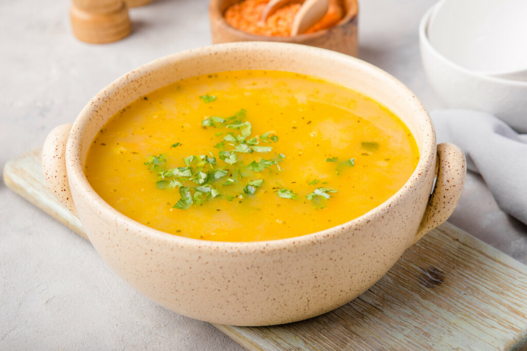 7 cremes e sopas funcionais para ajudar a emagrecer no inverno 6 Recipiente bege com sopa de cenoura polvilhada com coentro picado