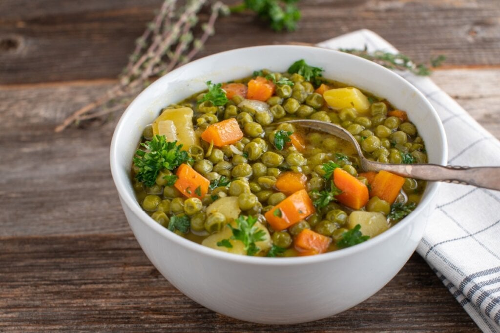 7 sopas proteicas para os dias frios 6 Sopa de ervilha com legumes servido em tigela de porcelana branca em cima de mesa de madeira
