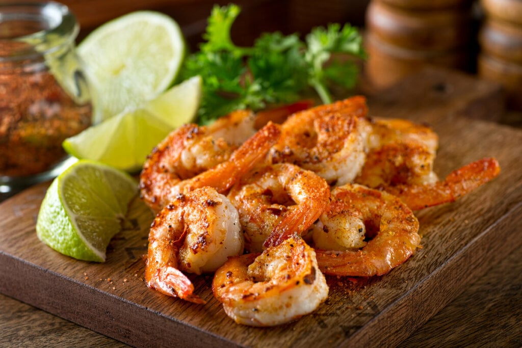 7 receitas ricas em proteínas para o almoço 6 Camarões grelhados em cima de uma tábua de madeira com rodelas de limão