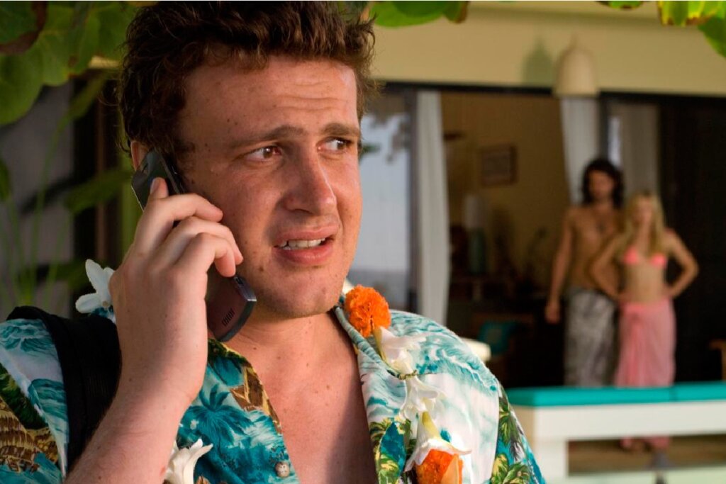 7 comédias românticas imperdíveis para o Dia dos Namorados 35 Jason Segel em uma cena no Havaí, falando ao telefone com uma expressão angustiada, com um casal ao fundo