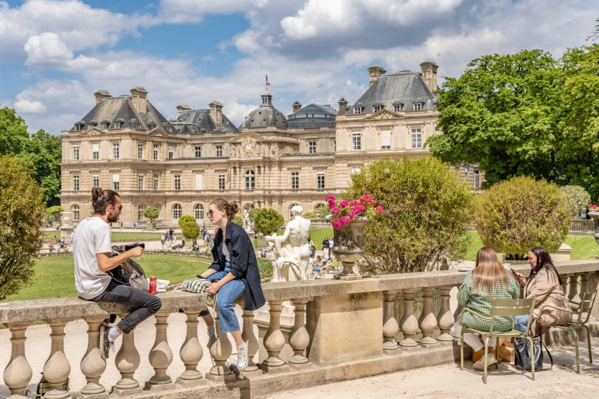 5 destinos românticos para visitar no Dia dos Namorados 23 Casais aproveitando o dia ensolarado nos Jardins de Luxemburgo em Paris, com palácio ao fundo