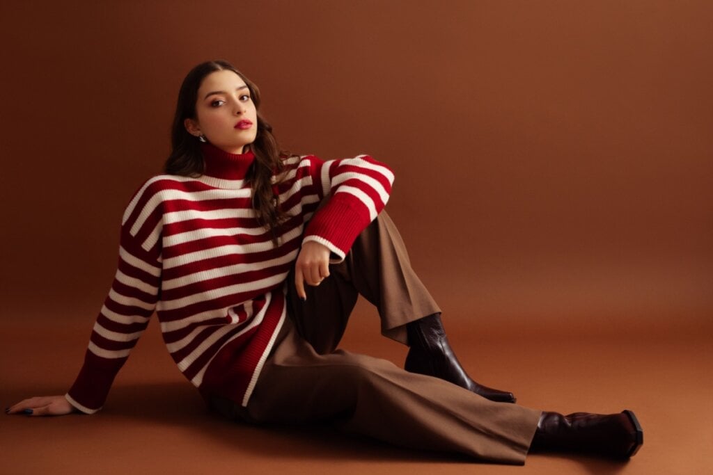5 tendências de moda casual para o inverno 22 Mulher com suéter listrado vermelho e branco, calça marrom e botas escuras posando