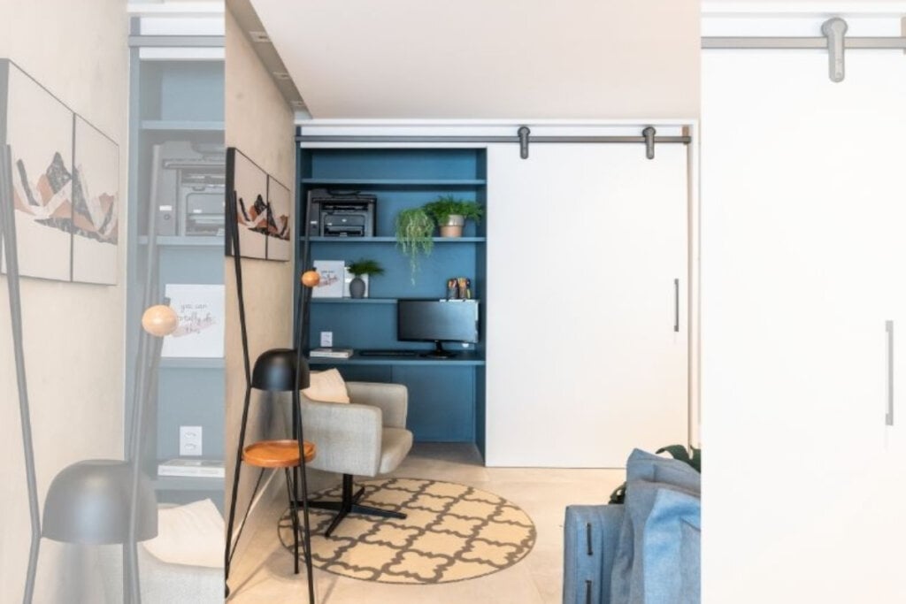 4 dicas para integrar o home office à sala de estar 17 imagem de homem office em tons de azul com cadeira cinza e porta de correr branca ao lado direito
