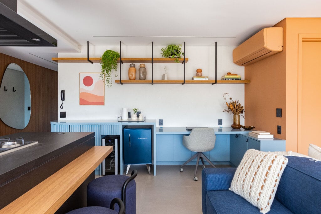 4 dicas para integrar o home office à sala de estar 16 imagem de sala de estar com sofá e poltronas azuis com bar e home office com armário azul-claro ao fundo e cadeira cinza
