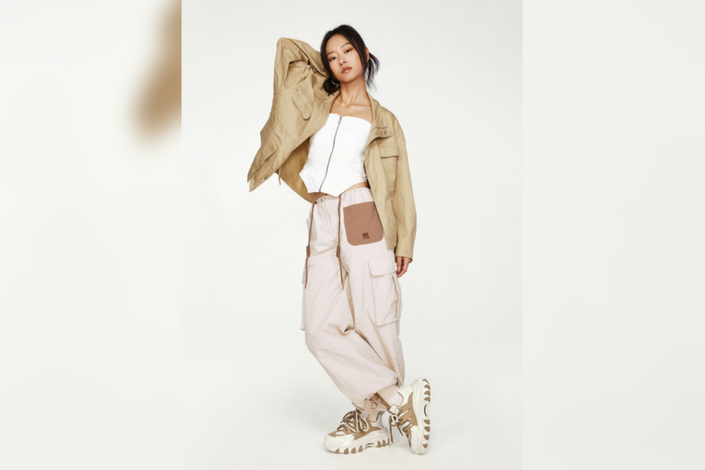 5 tendências de moda casual para o inverno 24 Mulher posando com jaqueta clara, calça cargo larga e tênis chunky em estúdio de fundo branco