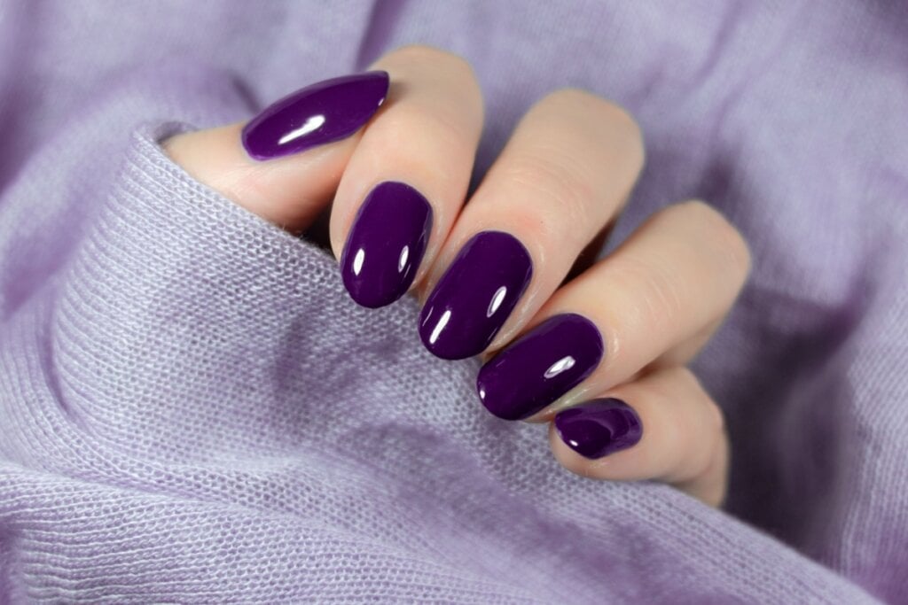 mão feminina com tecido roxo e unhas com esmalte roxo